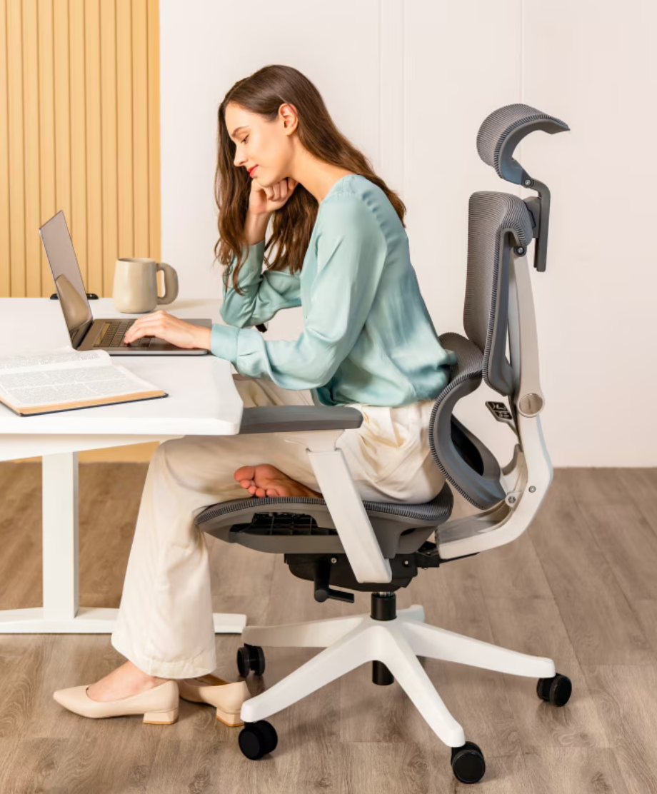 Woman working at a desk, seated in an ergonomic office chair, with a laptop and books