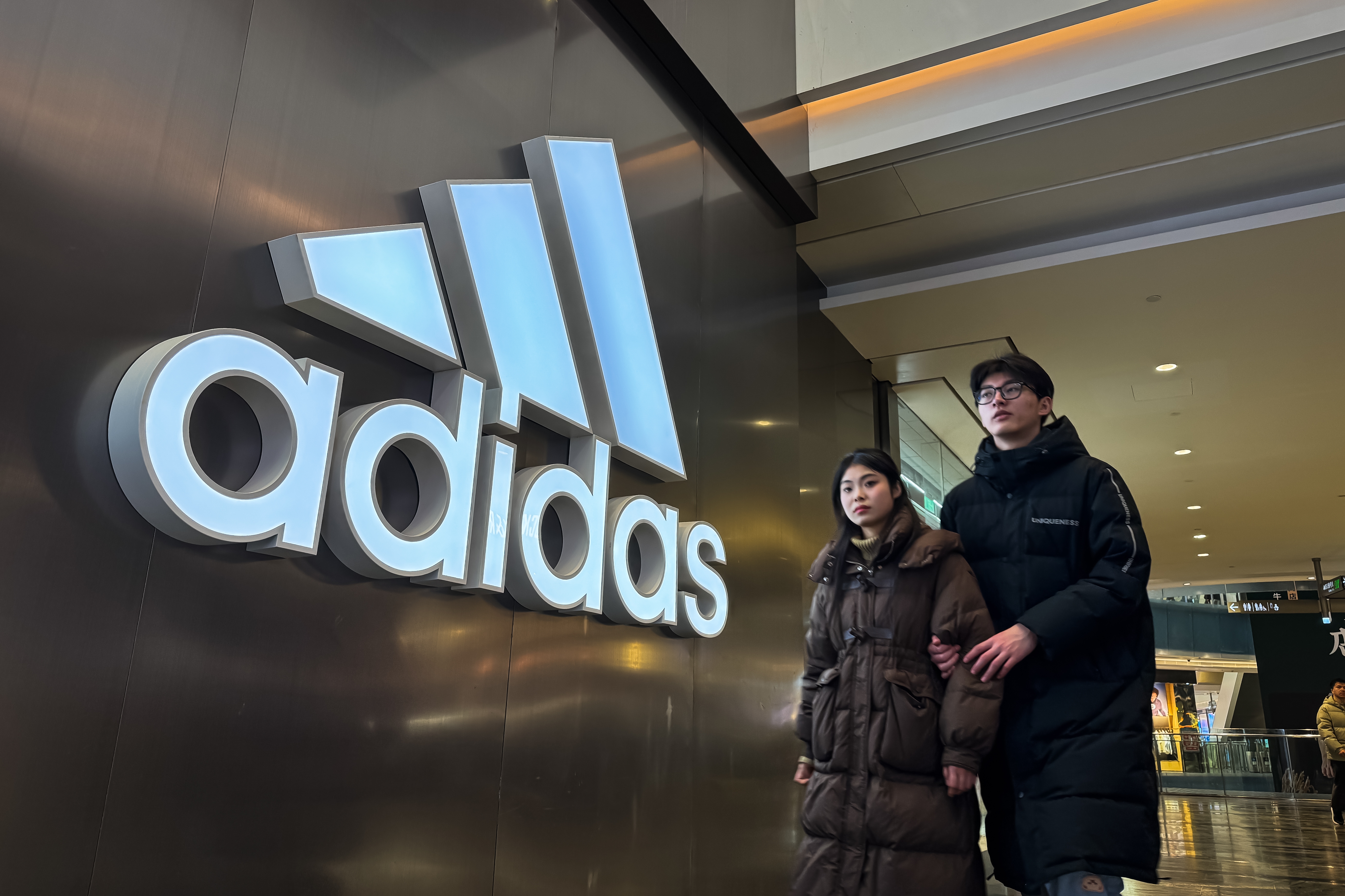 People walking past an Adidas store entrance inside a shopping mall