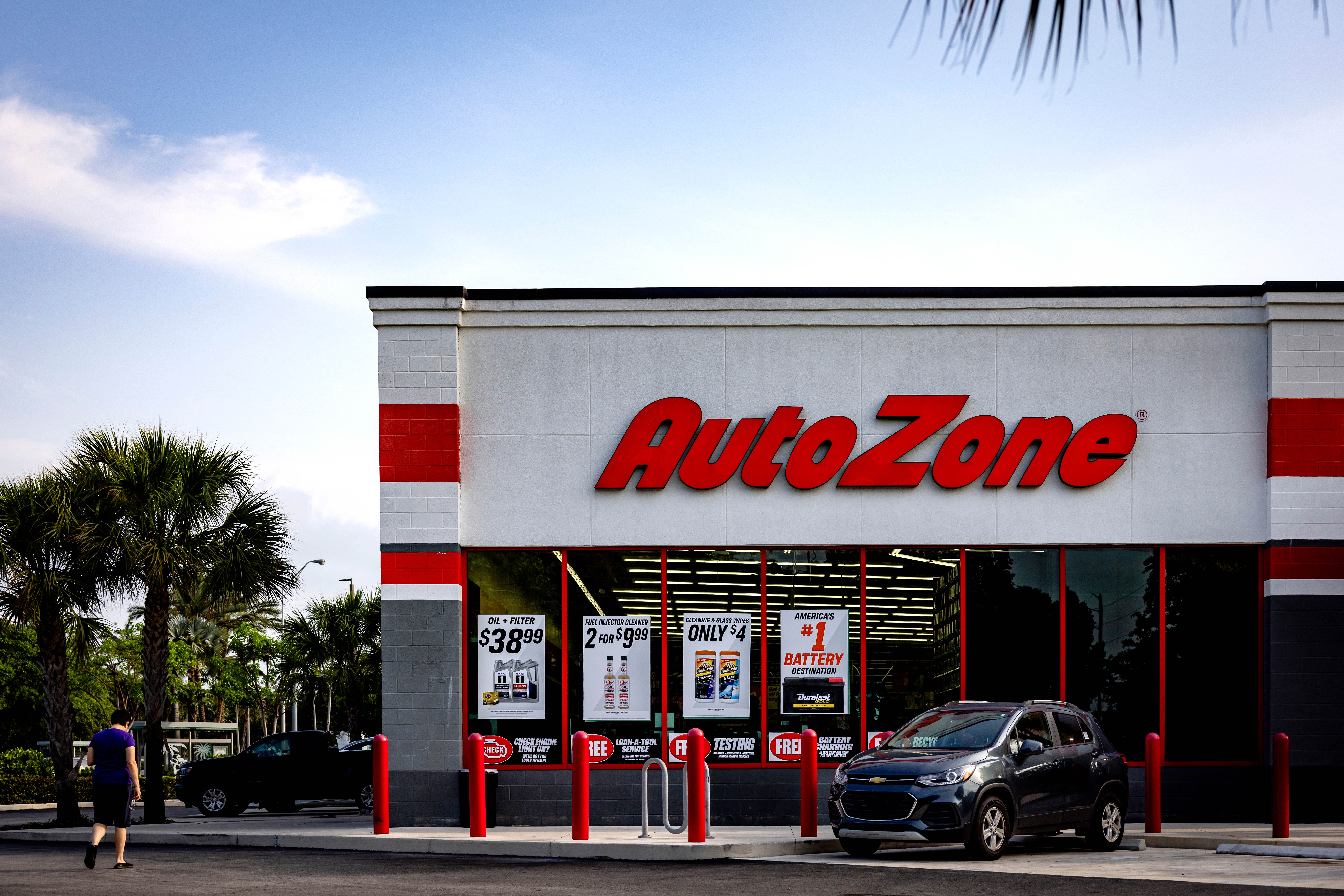 AutoZone storefront with promotional signs; a person walks in the parking lot beside parked cars