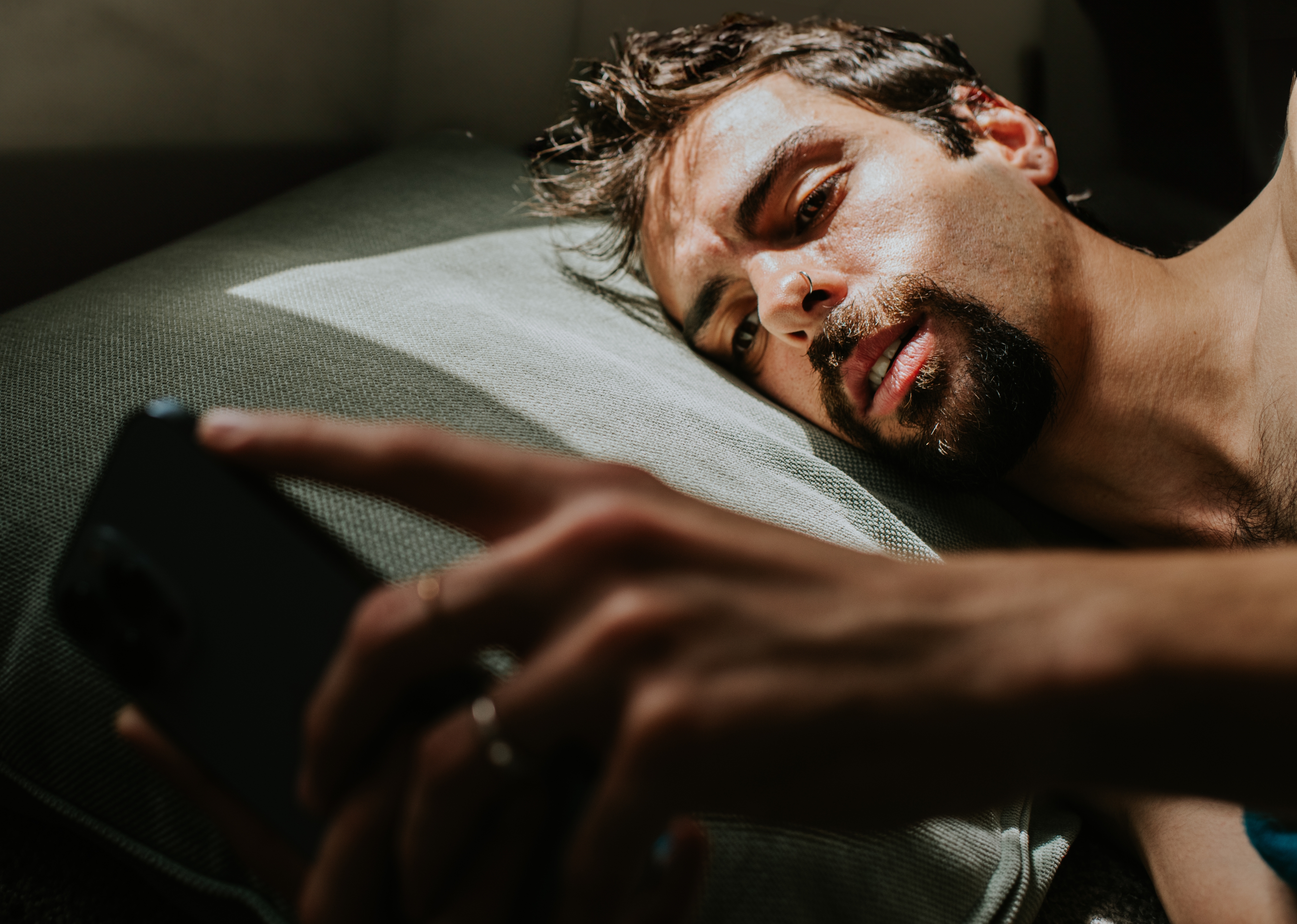 A man lies on a pillow, intently looking at his phone, suggesting a moment of contemplation or connection