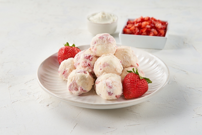 Plate of strawberry ice cream scoops garnished with fresh strawberries, with chopped strawberries and cream in the background