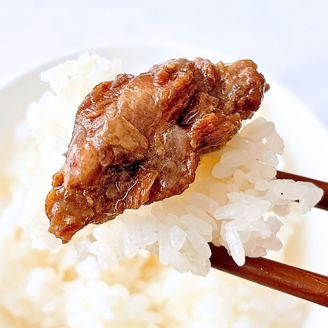 箸でご飯と焼肉を持ち上げた様子。ご飯の上に味付けされた肉が乗っています。食欲をそそるシーン。