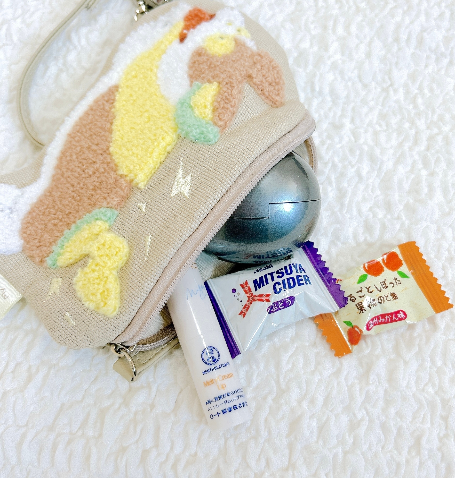 テーブルの上にぬいぐるみアート付きポーチ、薬、ミツヤサイダーのタブレット、キャンディーが置かれている。