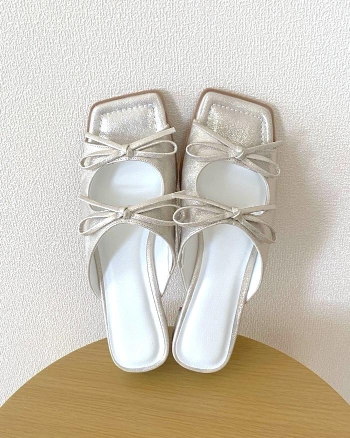 Pair of open-toe sandals with bows, resting on a wooden surface against a plain background