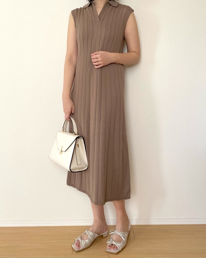 Person in a sleeveless, ribbed, knee-length dress holding a white handbag. Sandals with bow details complete the look