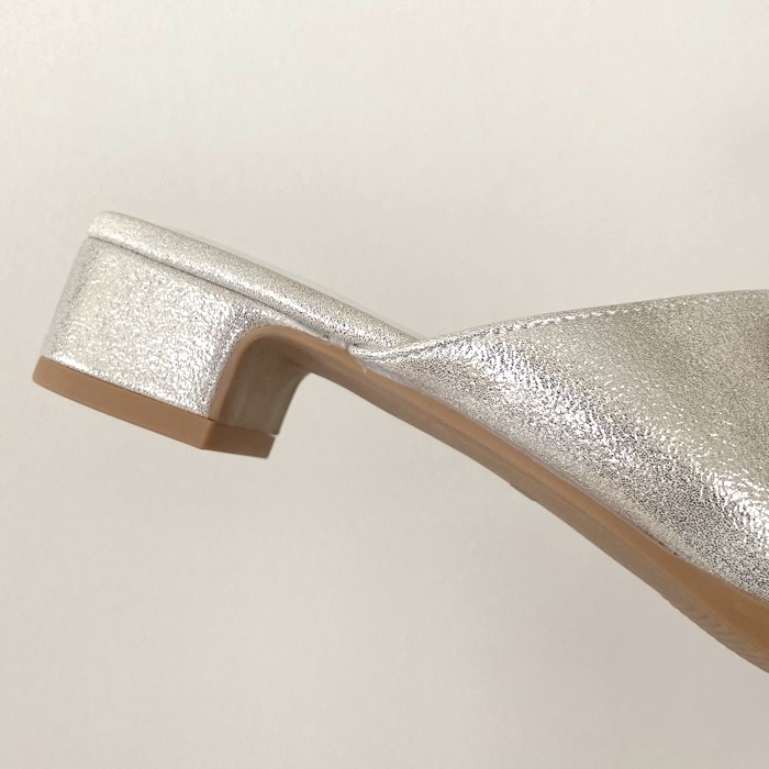 Silver metallic mule shoe with a low block heel, viewed from the side on a plain background