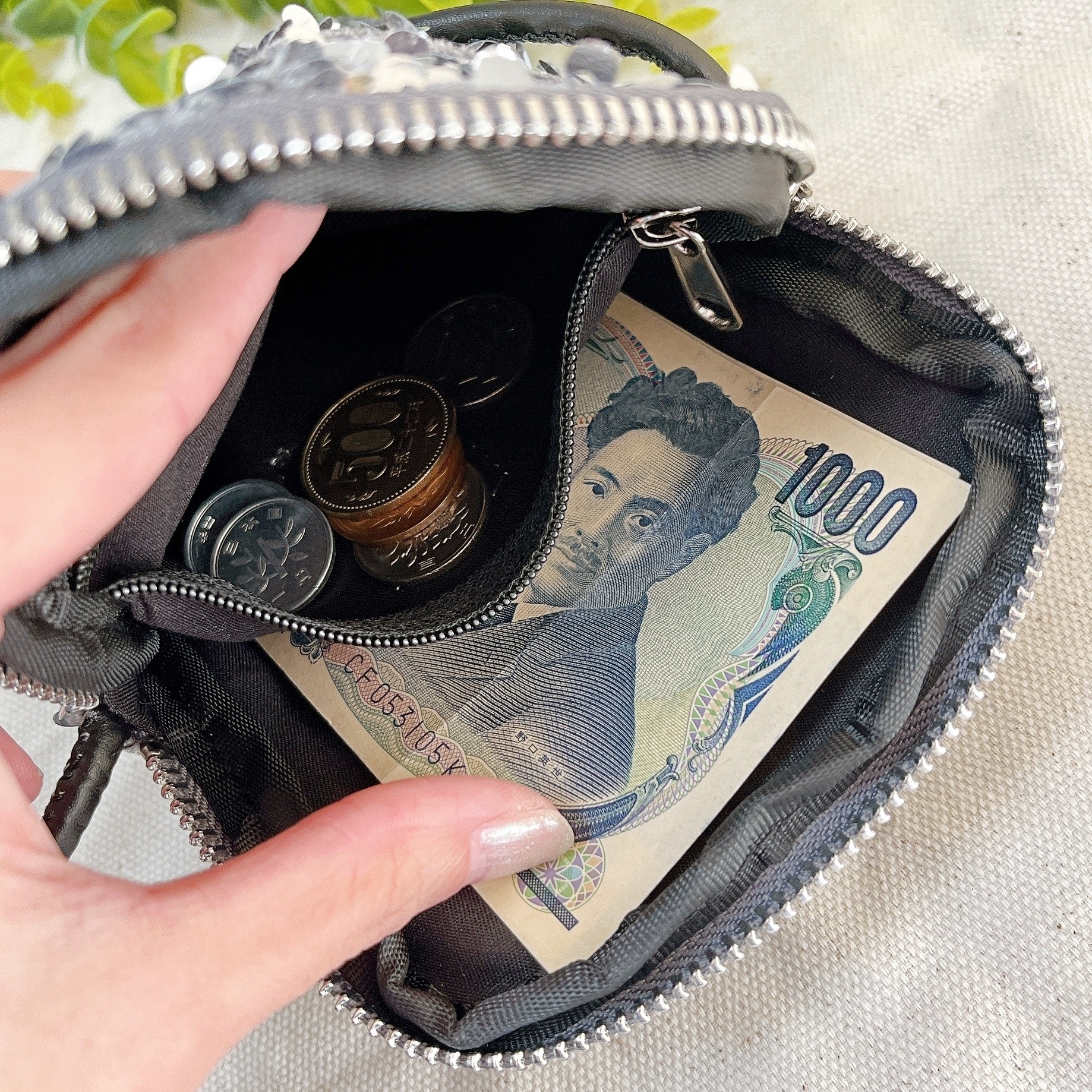 手の中の財布に1000円札と数枚の硬貨が入っています。