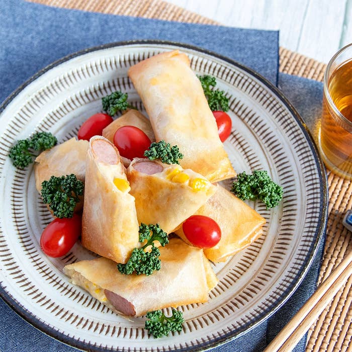 皿に盛り付けられた春巻き。トマトとハーブが添えられており、ガラスの飲み物が隣に置かれている。