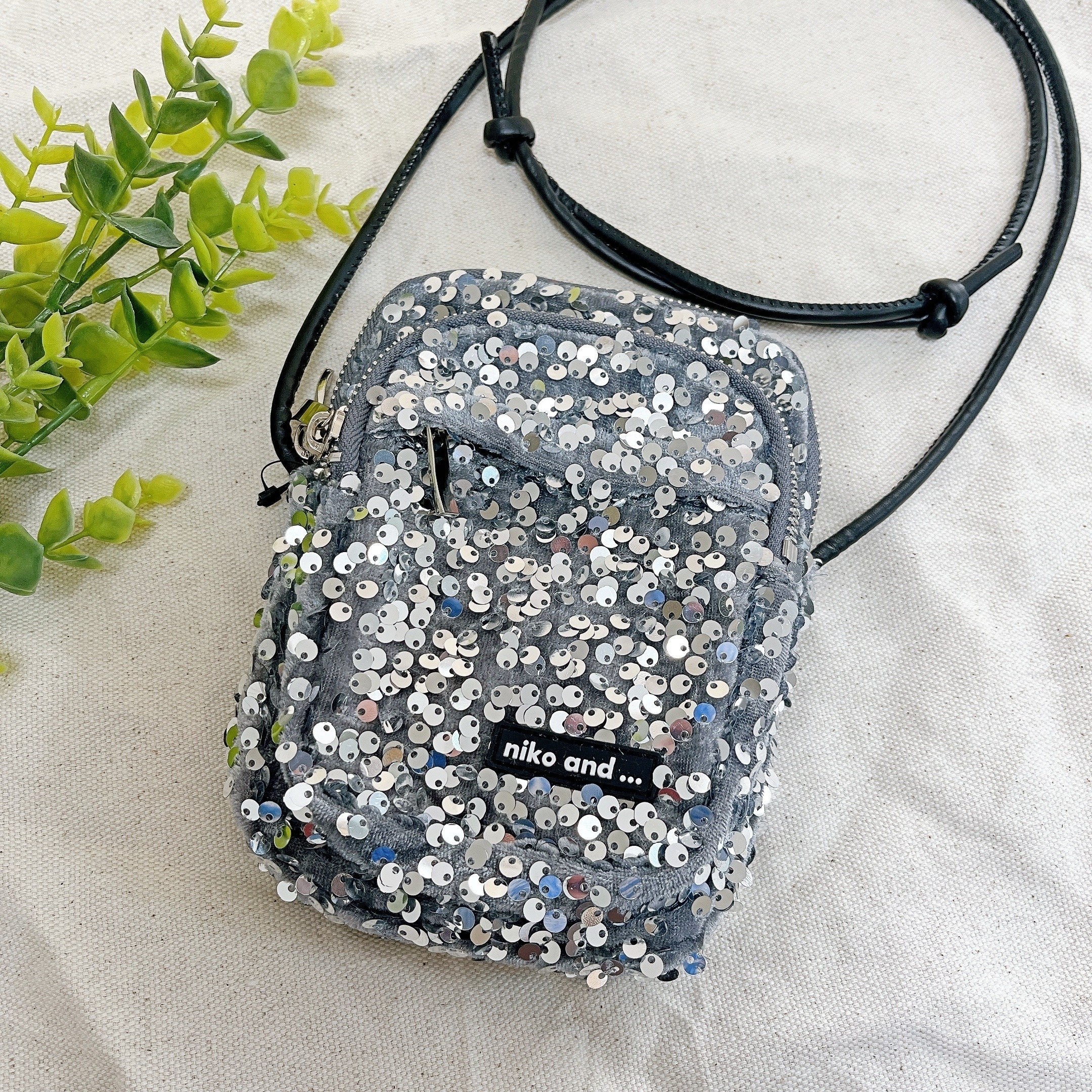 スパンコールで覆われた小さなクロスボディバッグ。人工植物が隣に置かれている。