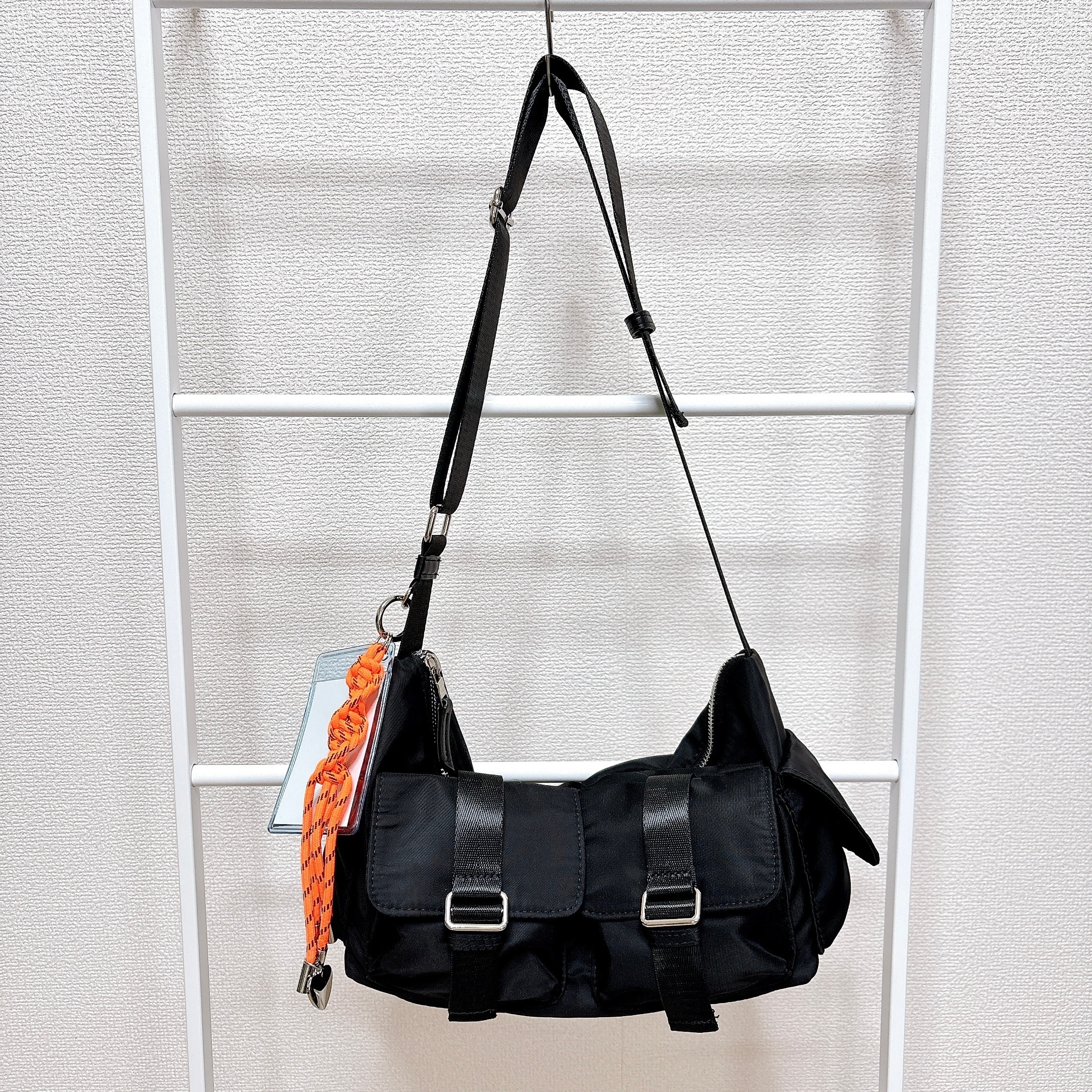 黒のショルダーバッグが掛けられている。バックルあり。バッグにはオレンジのチャームが付いている。