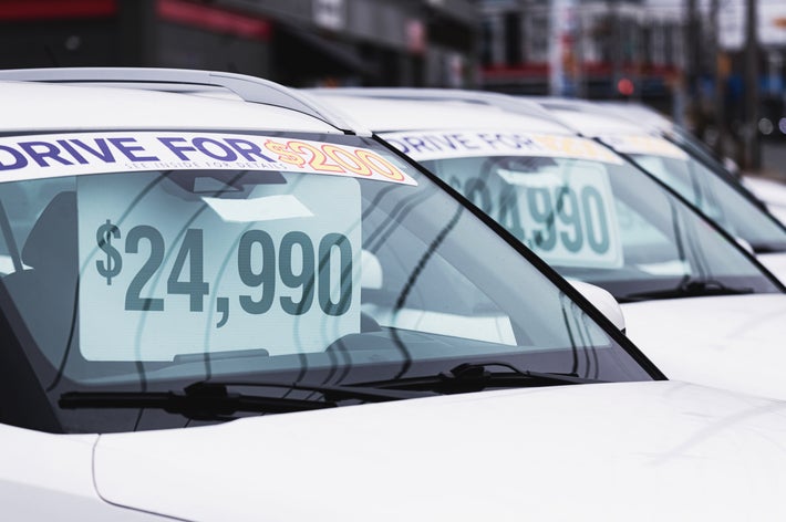 駐車場に並ぶ数台の車のフロントガラスに、価格が表示されたステッカーが貼られている。