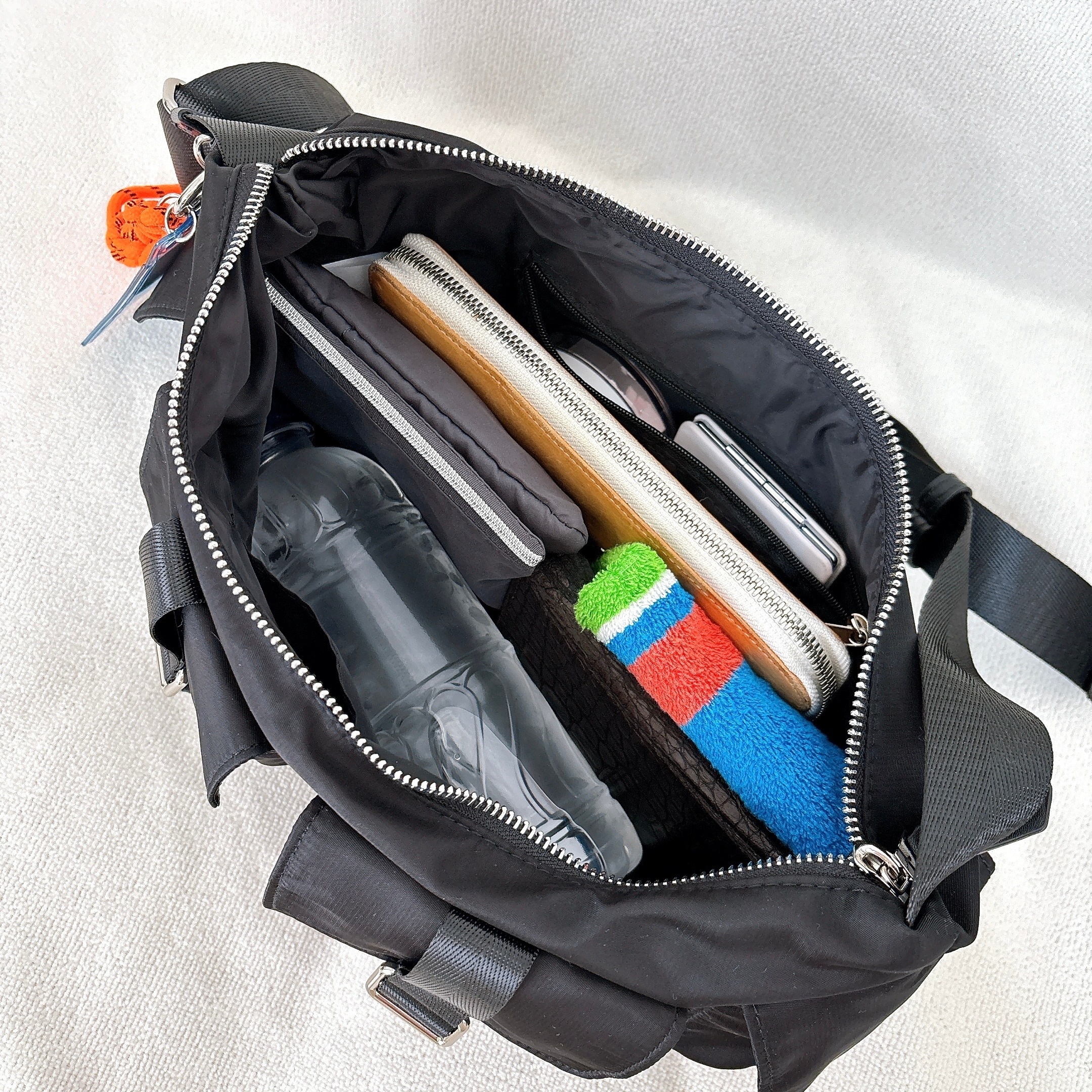 黒いバッグの中に、水のボトル、ノート、タブレット、財布、スマホ、カラフルなタオルが入っている。