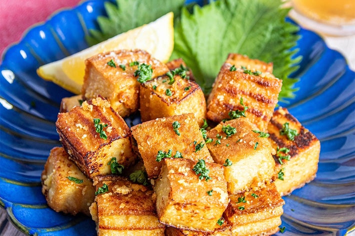 青い皿に盛られたグリルされた厚揚げのキューブ。トッピングされたパセリとレモンの輪切りが添えられている。