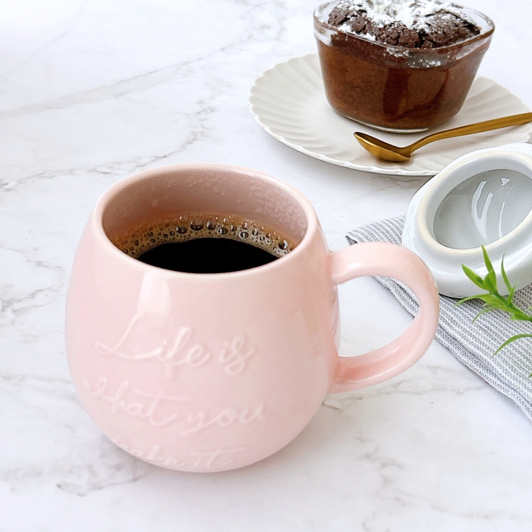 カップにコーヒーが注がれたテーブルの上に、ケーキが置かれています。カップには「Life is what you make it」の文字があります。