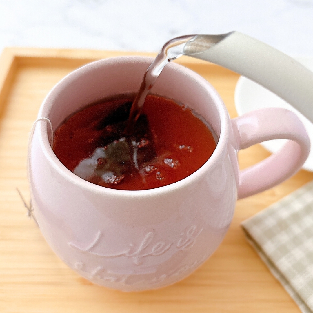 白いポットからマグカップに紅茶が注がれている。マグカップには「Life is」と書かれている。