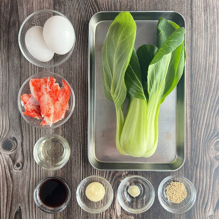 調理前の具材がテーブルに並べられている。卵、葉野菜、かにかまぼこ、調味料が小皿に入れてセットされている。