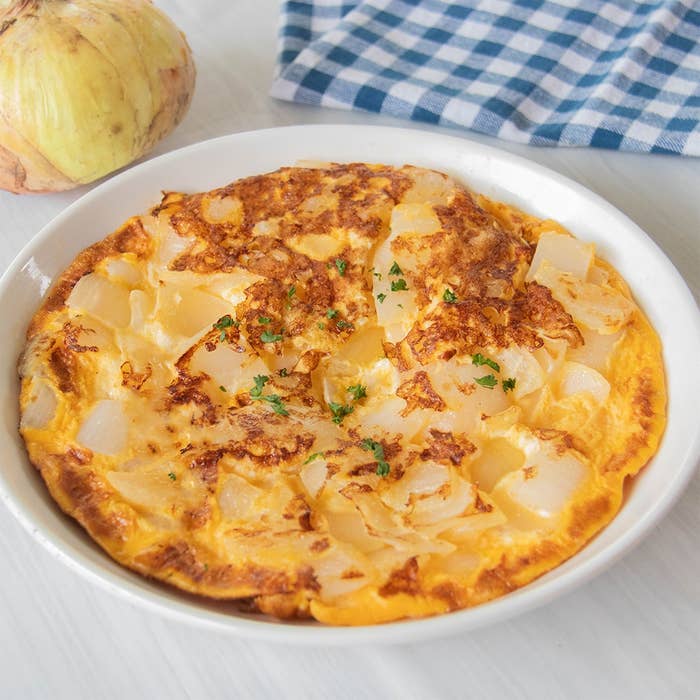 オムレツが白い皿に盛られ、角切りの玉ねぎが入っている。背景にチェック柄の布。