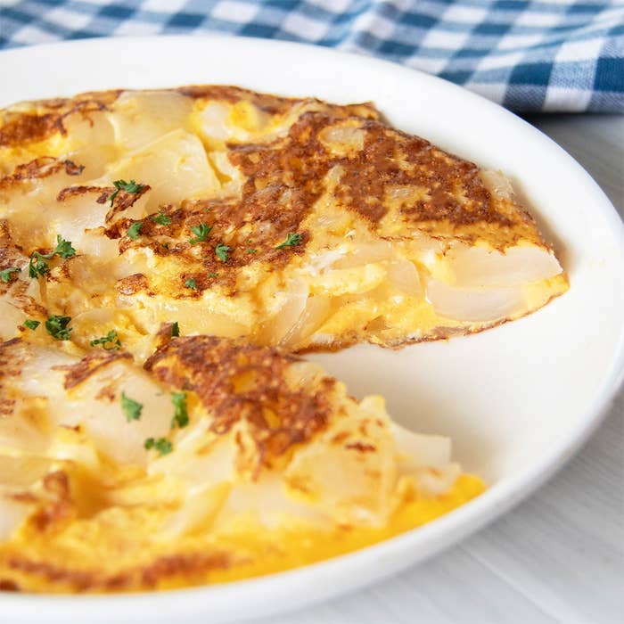 オムレツが白い皿に載せられている。上にはパセリが飾られている。背景にチェック柄の布が見える。