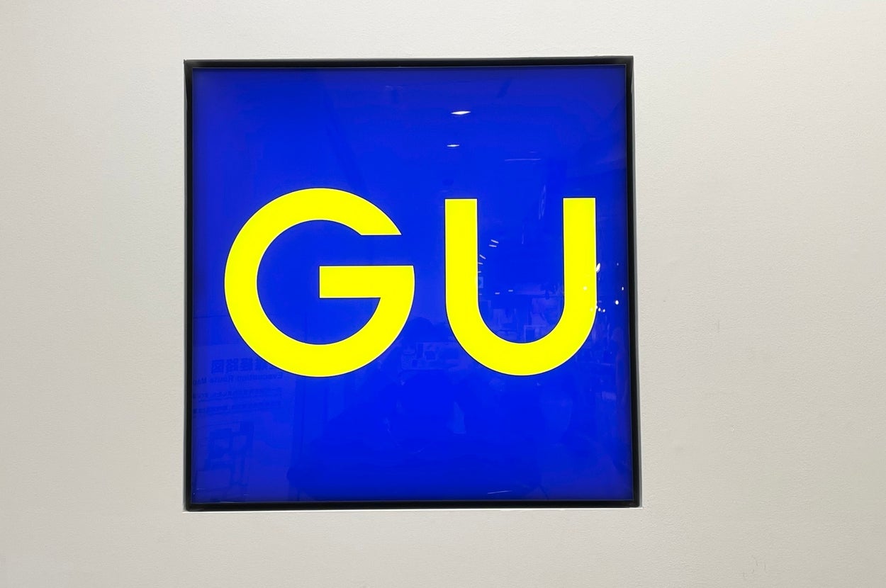 The image shows a square blue sign with large yellow letters "GU" in the center