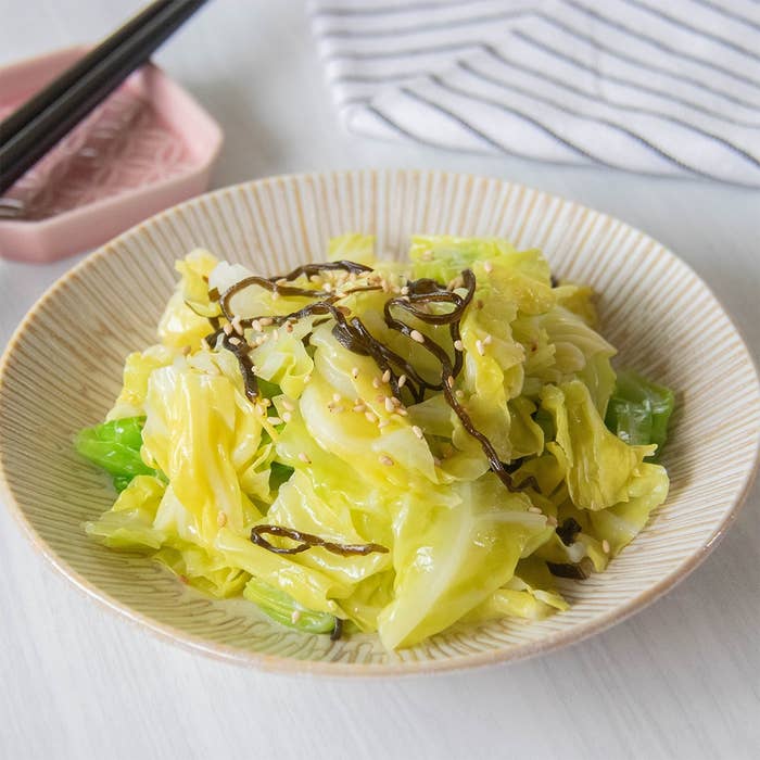 皿に盛られたゆでたキャベツのサラダ、昆布とゴマでトッピング。背景に箸と布がある。