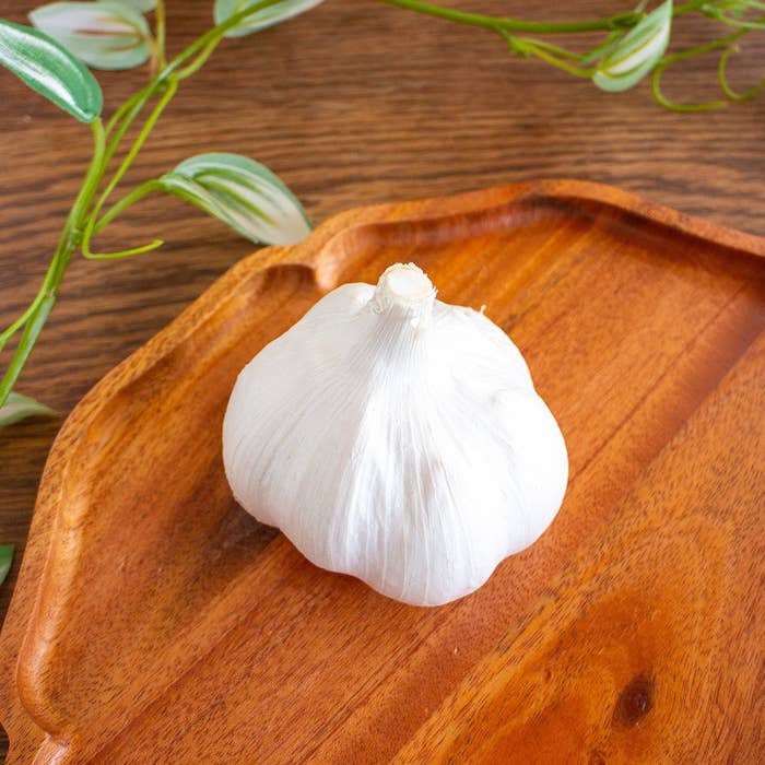 木のトレイに乗ったニンニクの頭。背景には葉の一部が見える。