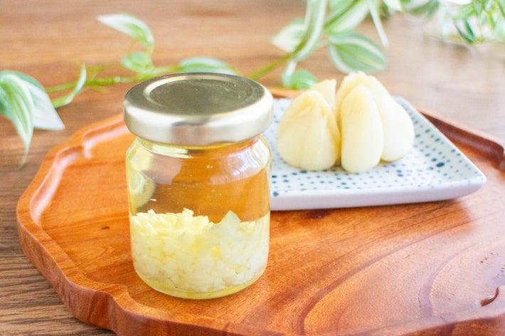 木製トレー上に、瓶詰めにされた刻んだにんにくと皿に盛られた漬けにんにく。バックに観葉植物。