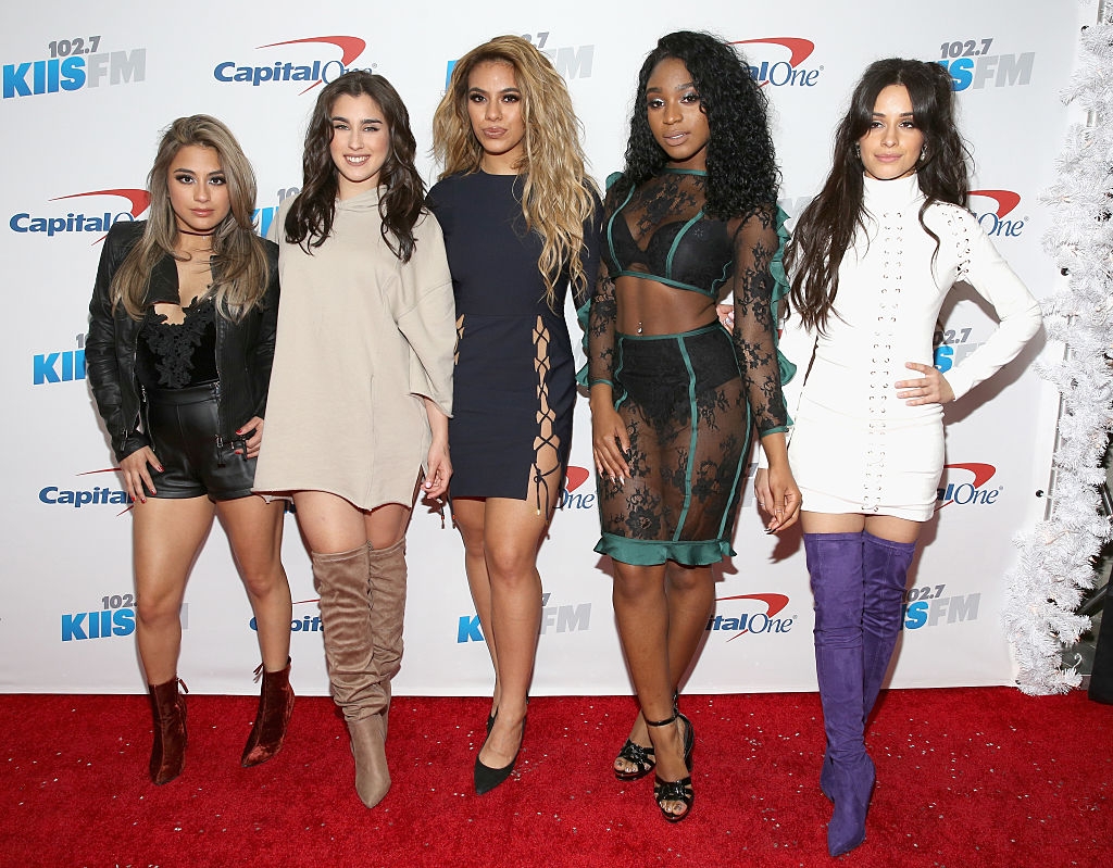 Five women pose on a red carpet in stylish outfits featuring mini dresses and thigh-high boots at a KIIS FM and Capital One event