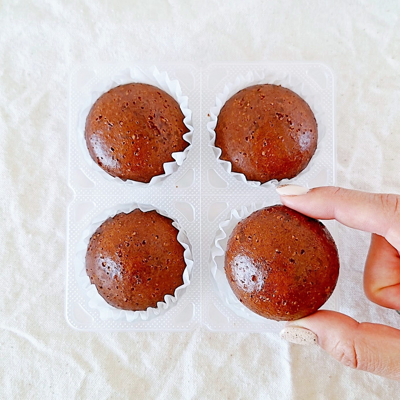 手が4つのチョコレートブラウニーを持ち上げようとしている。プラスチック容器に入っている。