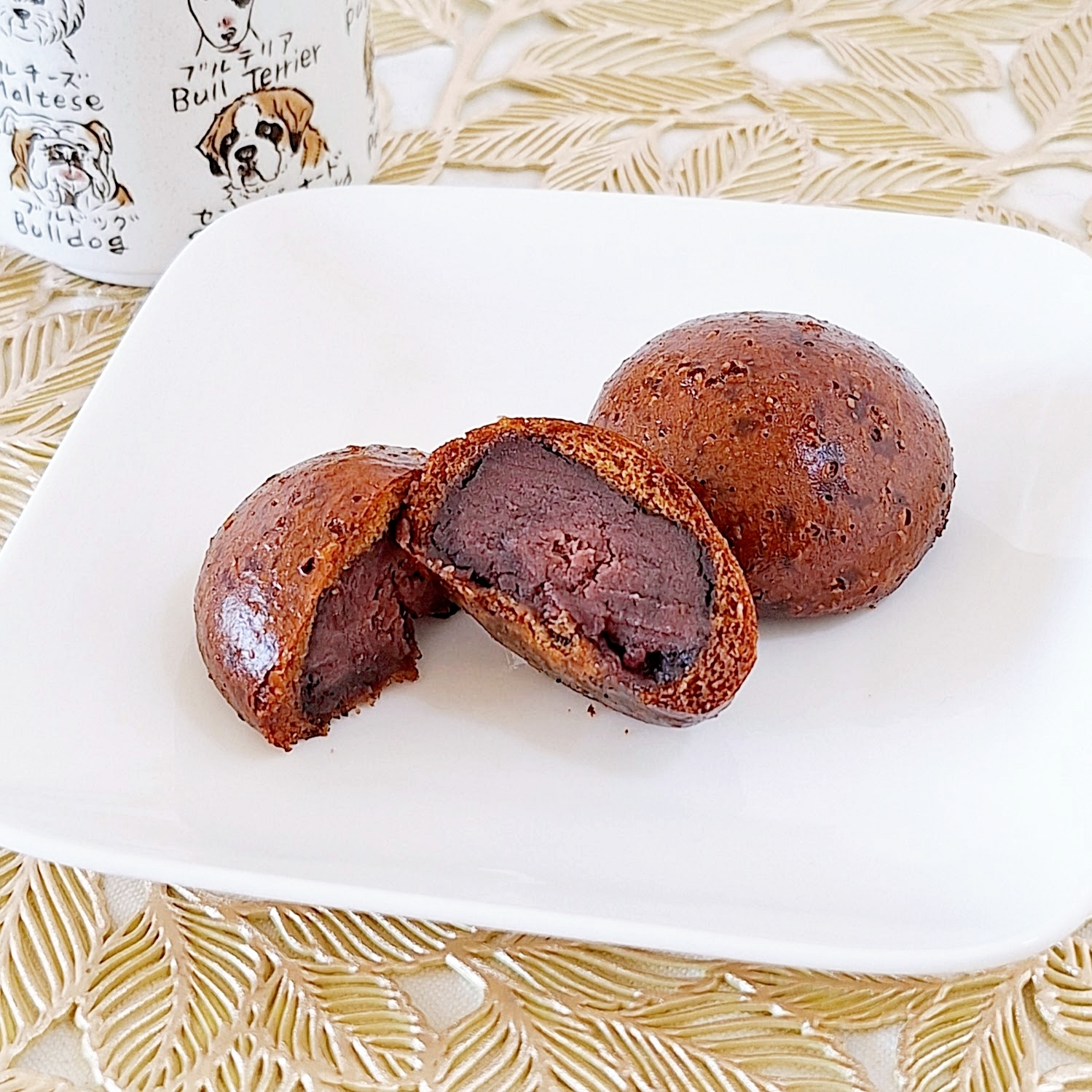 白い皿にあんこが入った焼き菓子が3つ。1つは半分に切られて中が見えています。背景に犬の絵が描かれたカップ。