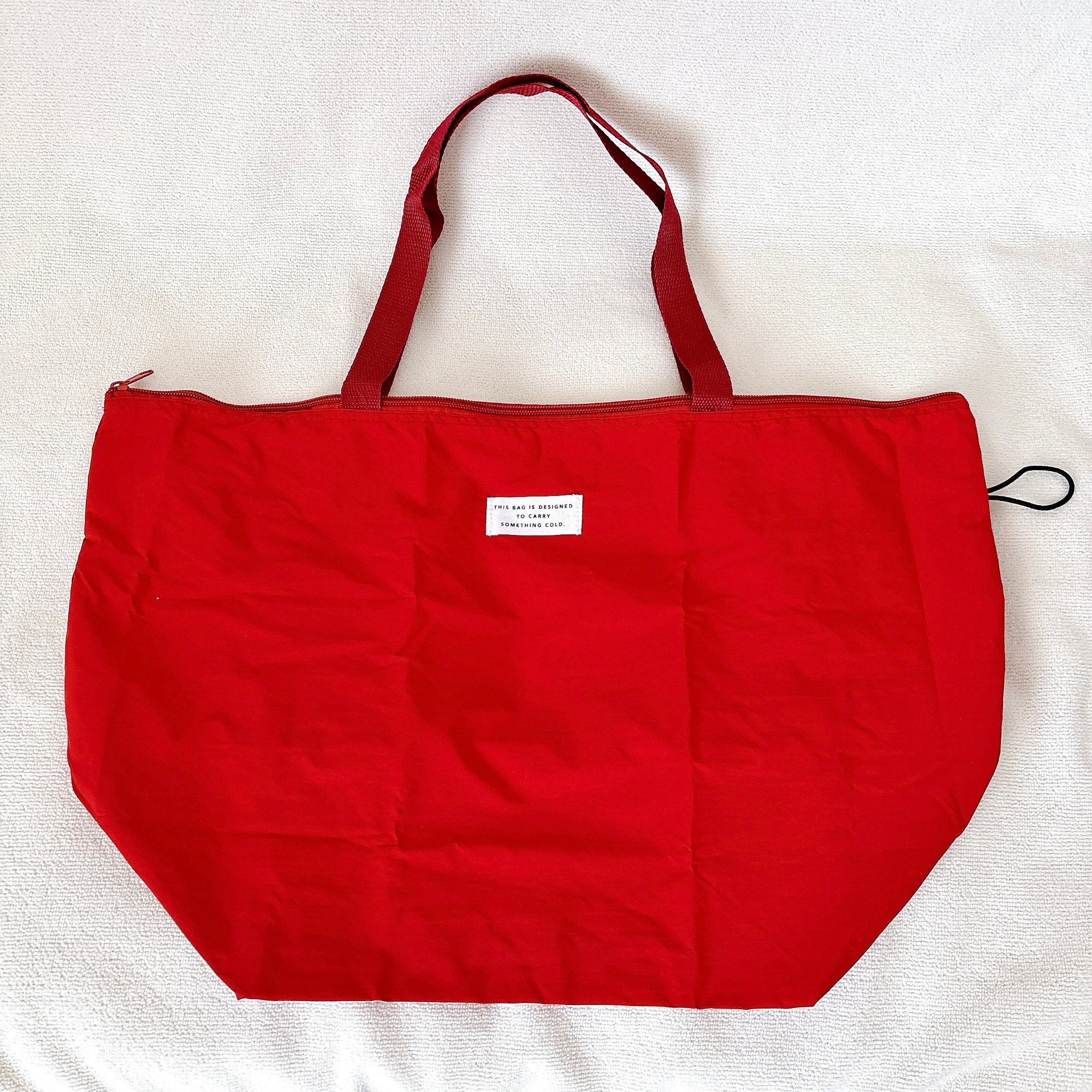 赤いトートバッグが白い背景に置かれています。中央上部に小さなタグが付いています。