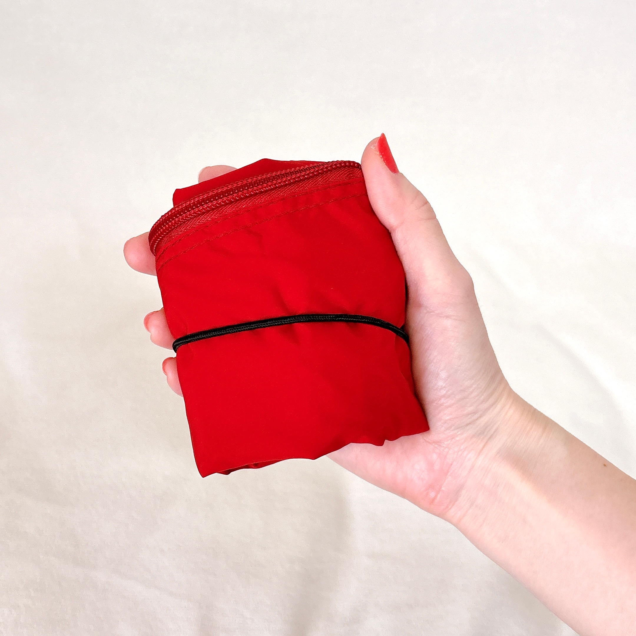 手に持たれた赤い折り畳み袋。収納用ゴムバンドが巻かれています。