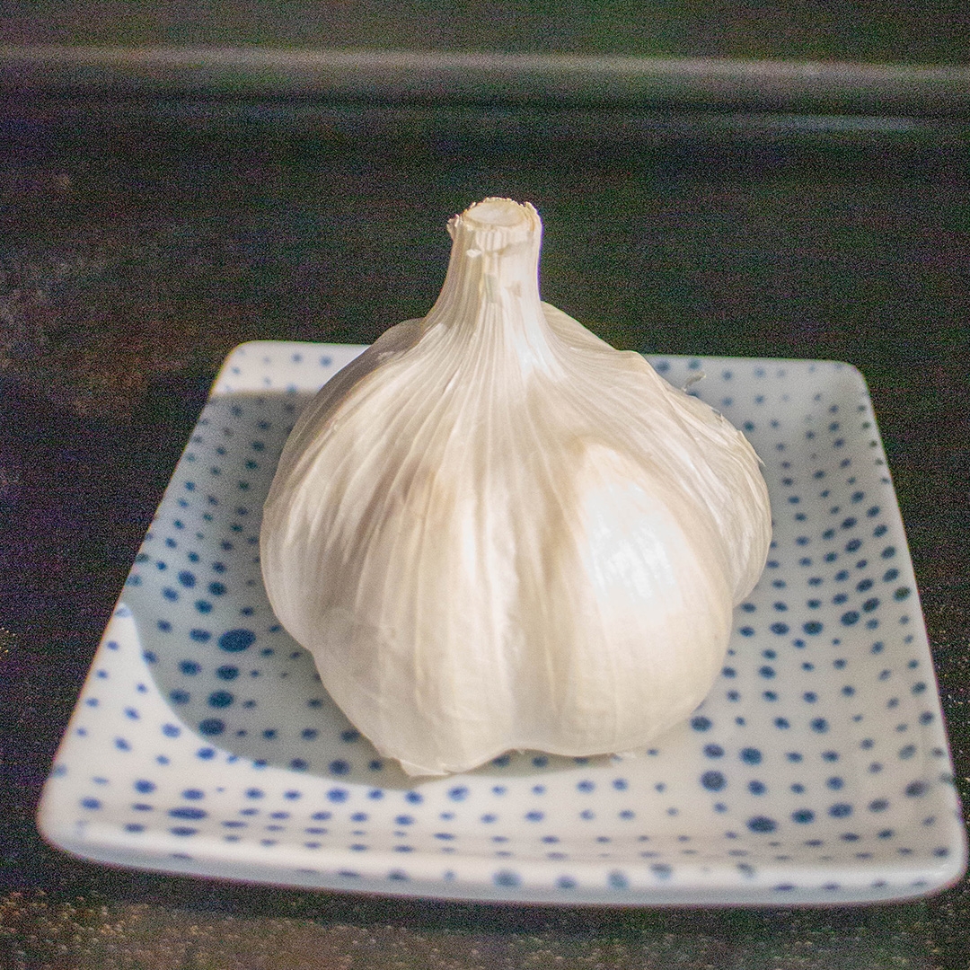 白いセラミック皿に盛られた一房のニンニク。シンプルでクリーンな食材のディスプレイ。