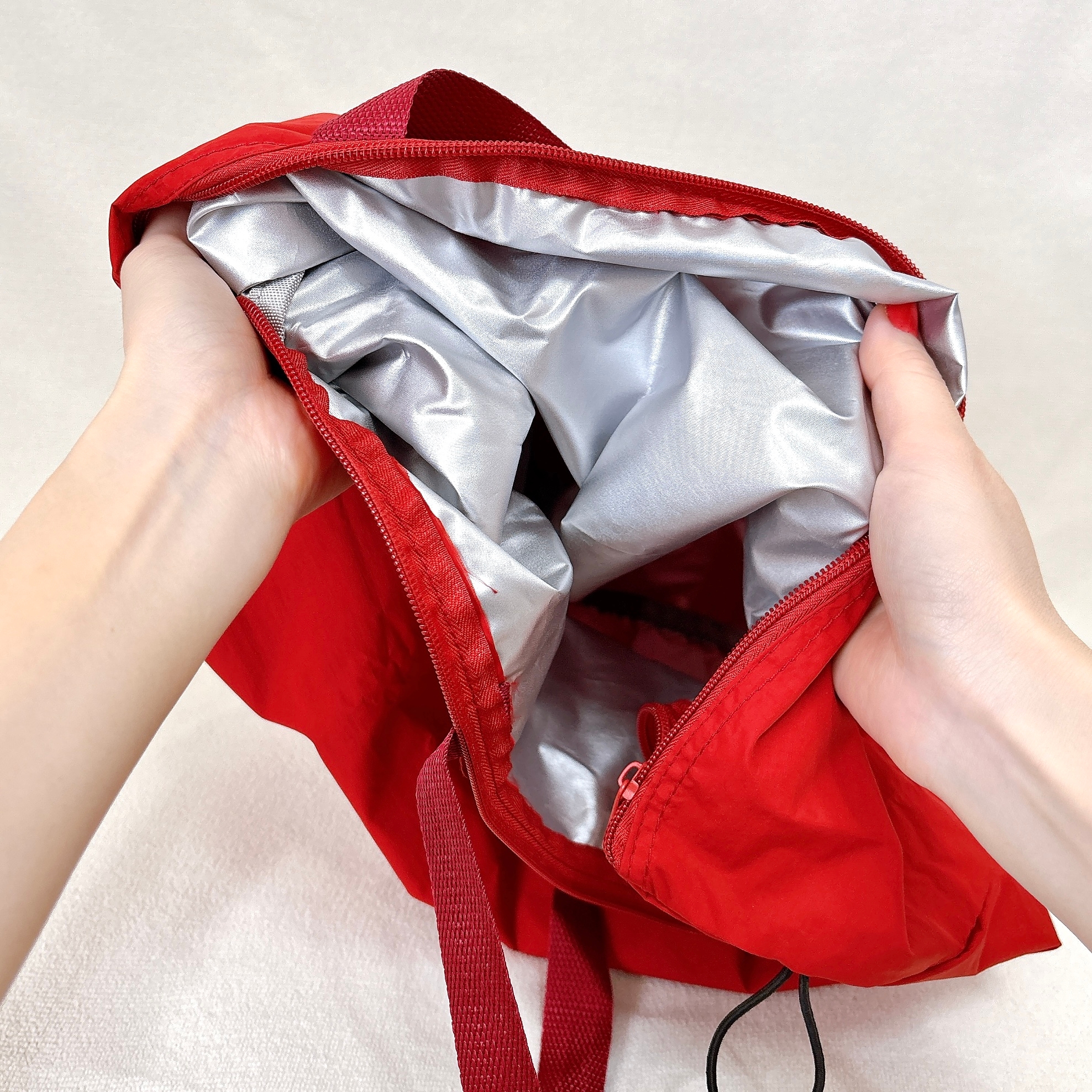 赤いバッグの内側が写っており、ハンドルを持つ手が見える。内側は銀色のライナーで覆われている。バッグのデザインが特徴的。