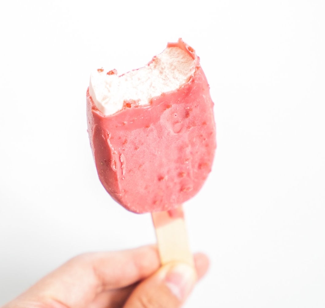 かじりかけのアイスキャンディーを持つ手。シンプルで清潔な背景。