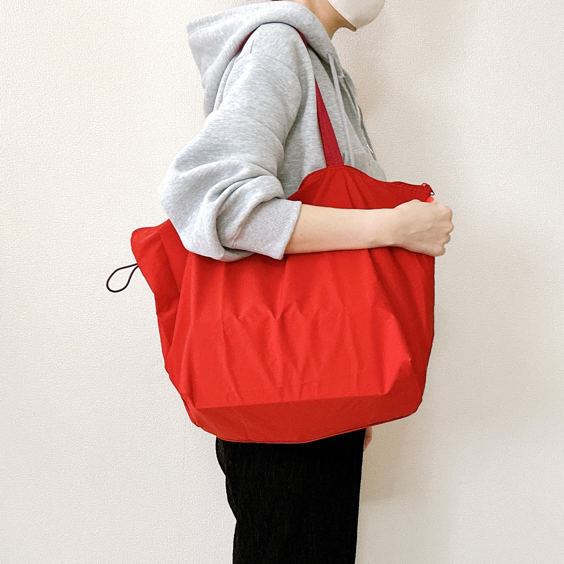 フード付きトレーナーを着た人物が、大きな赤いバッグを肩にかけている横向きの写真。