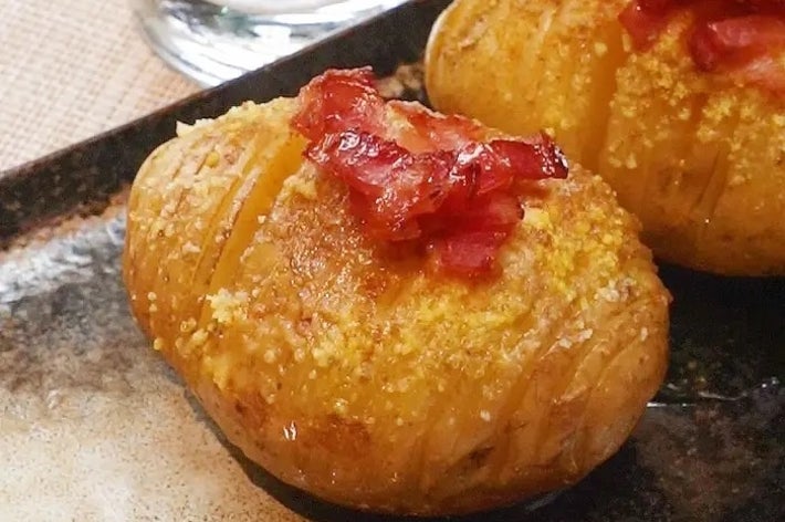 ベイクドポテトにベーコンを載せた料理が皿に盛られ、ガラスの水が背景にある。