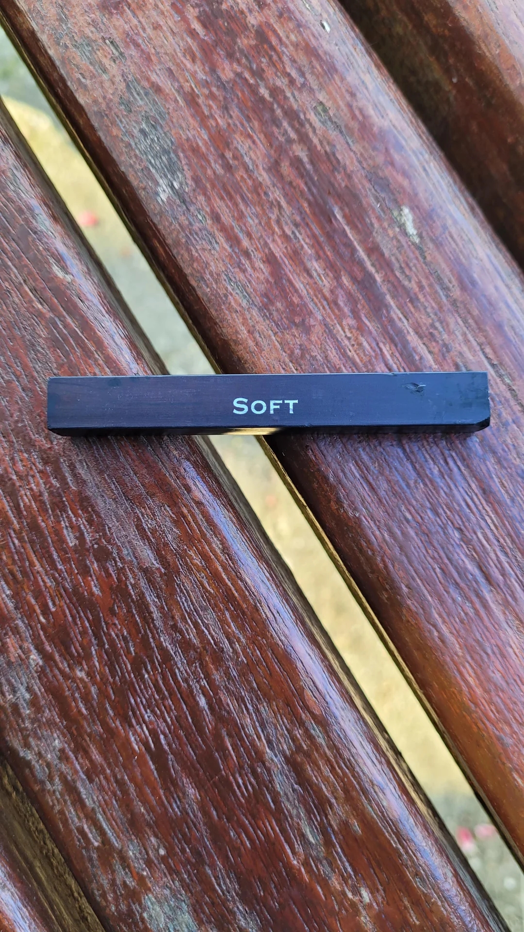 A black charcoal labeled "SOFT" resting on a wooden bench