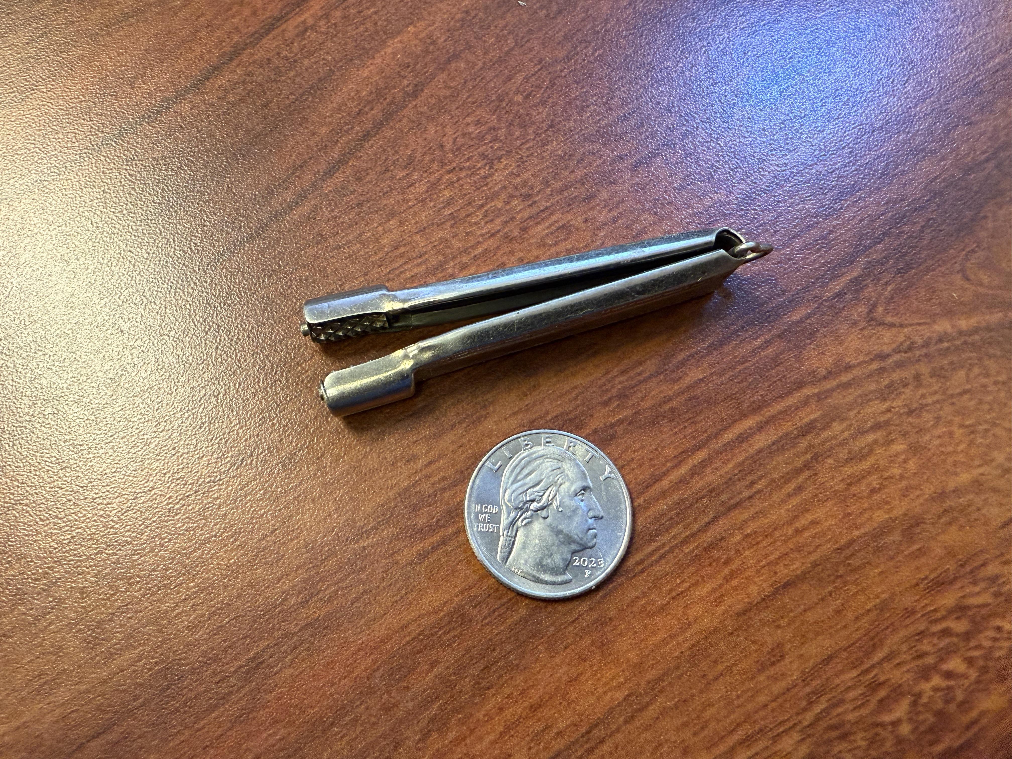 Metal tool with textured end beside a 2021 U.S. quarter on a wooden surface