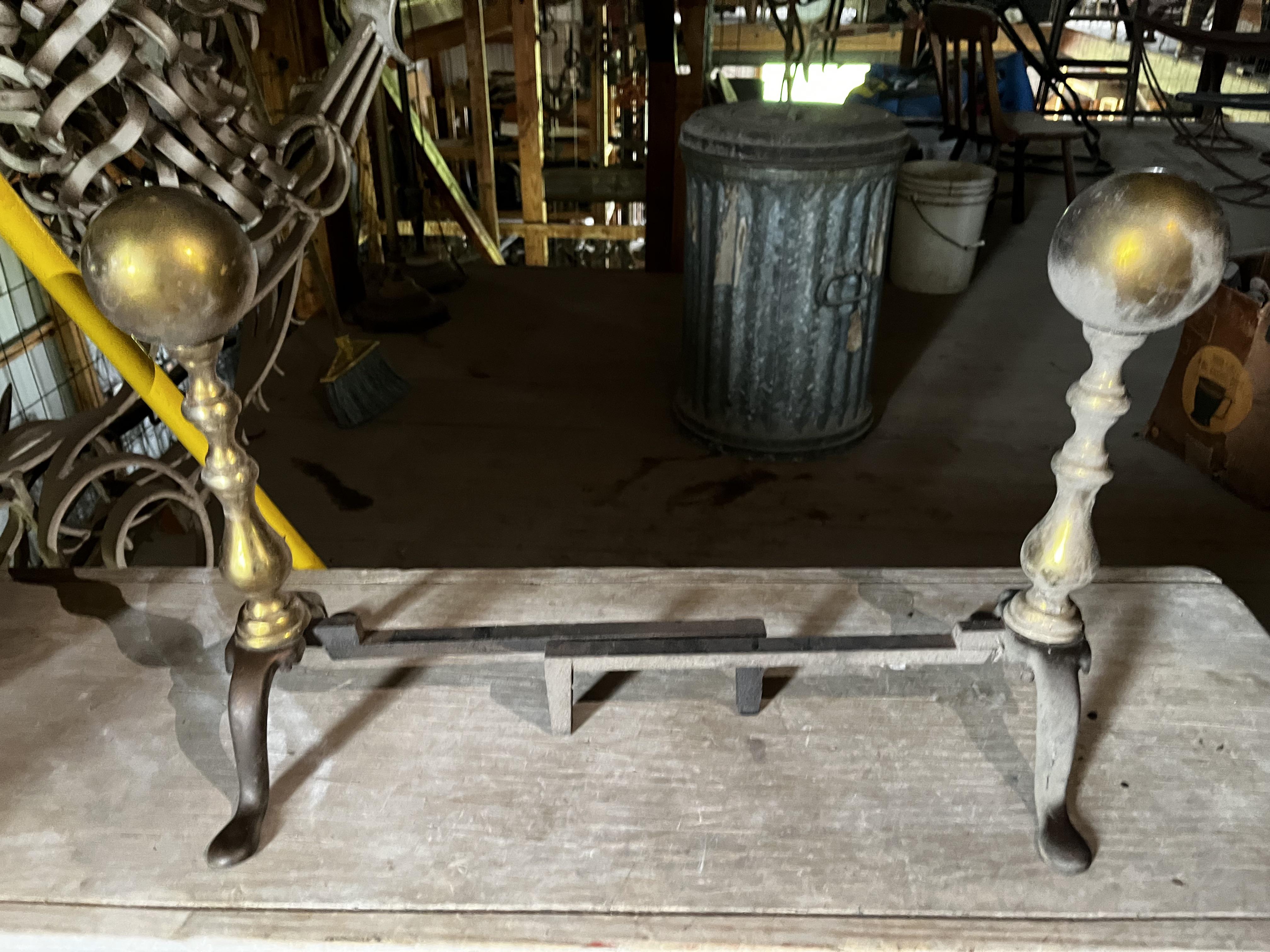 Metal fireplace andirons with spherical tops in a rustic setting. Logs and miscellaneous items are in the background