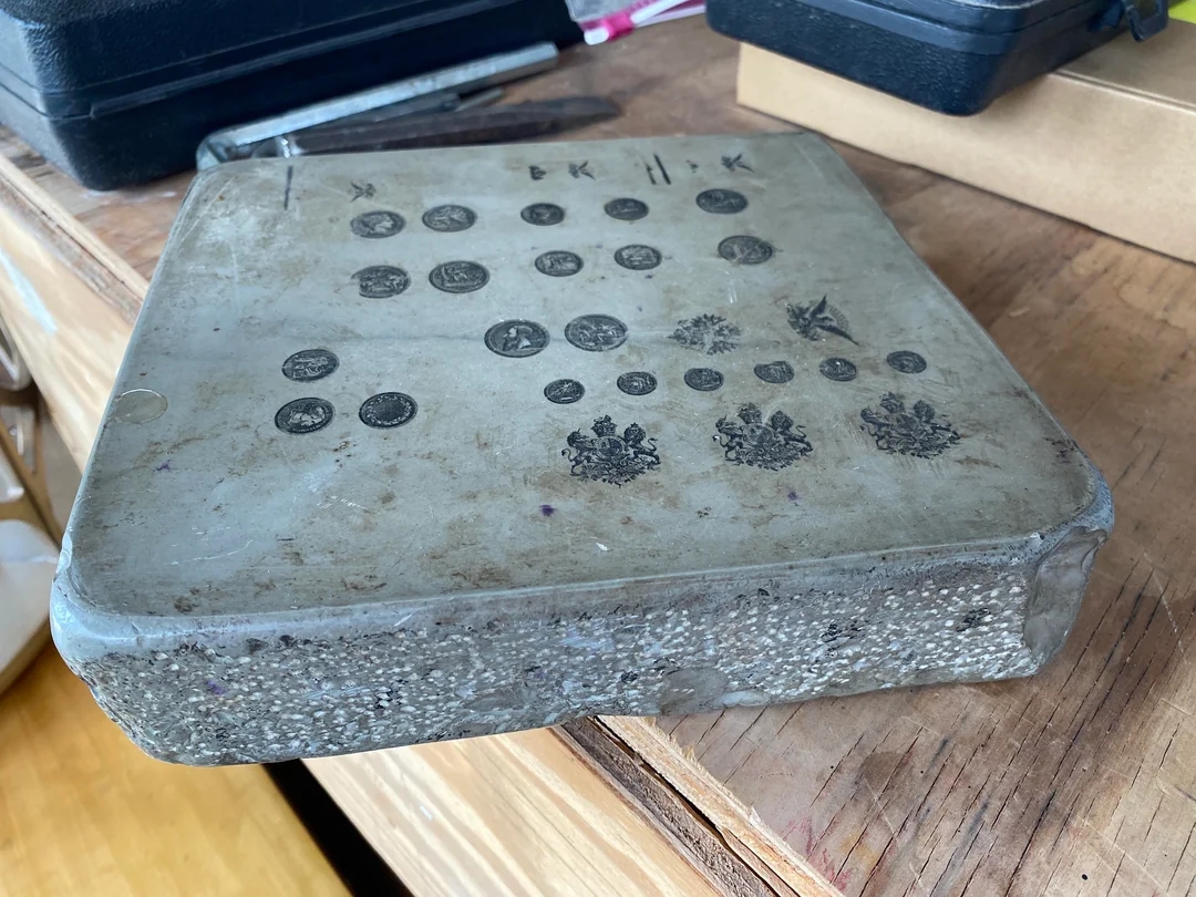 Rectangular metal plate with engravings of various coins and emblem designs on a wooden surface