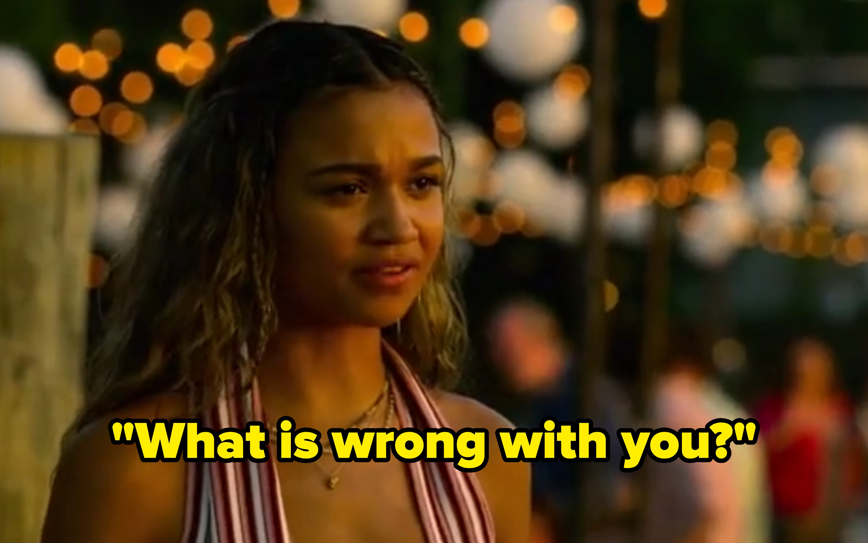 Person outdoors at an evening event, wearing a striped halter top and layered necklaces, with string lights in the background