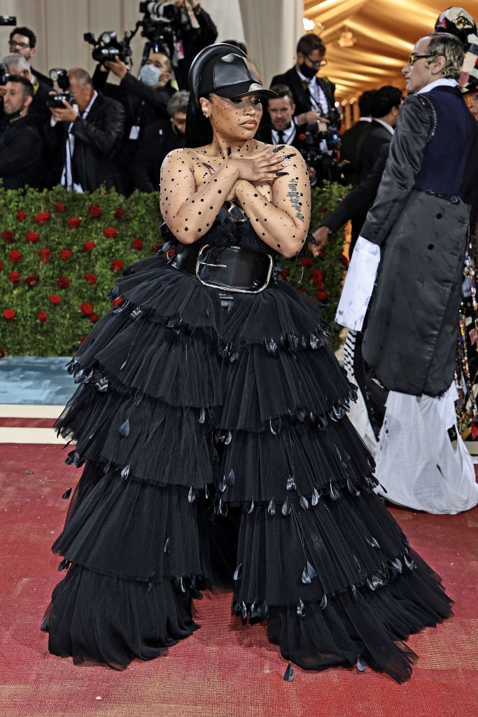 Nicki in a dramatic tiered gown with a large belt detail and matching cap, posing with her arms crossed over her chest