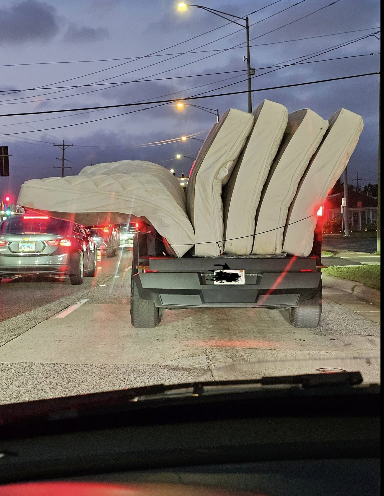 Truck transporting several large mattresses stacked upright on its open bed at night. Traffic seen ahead