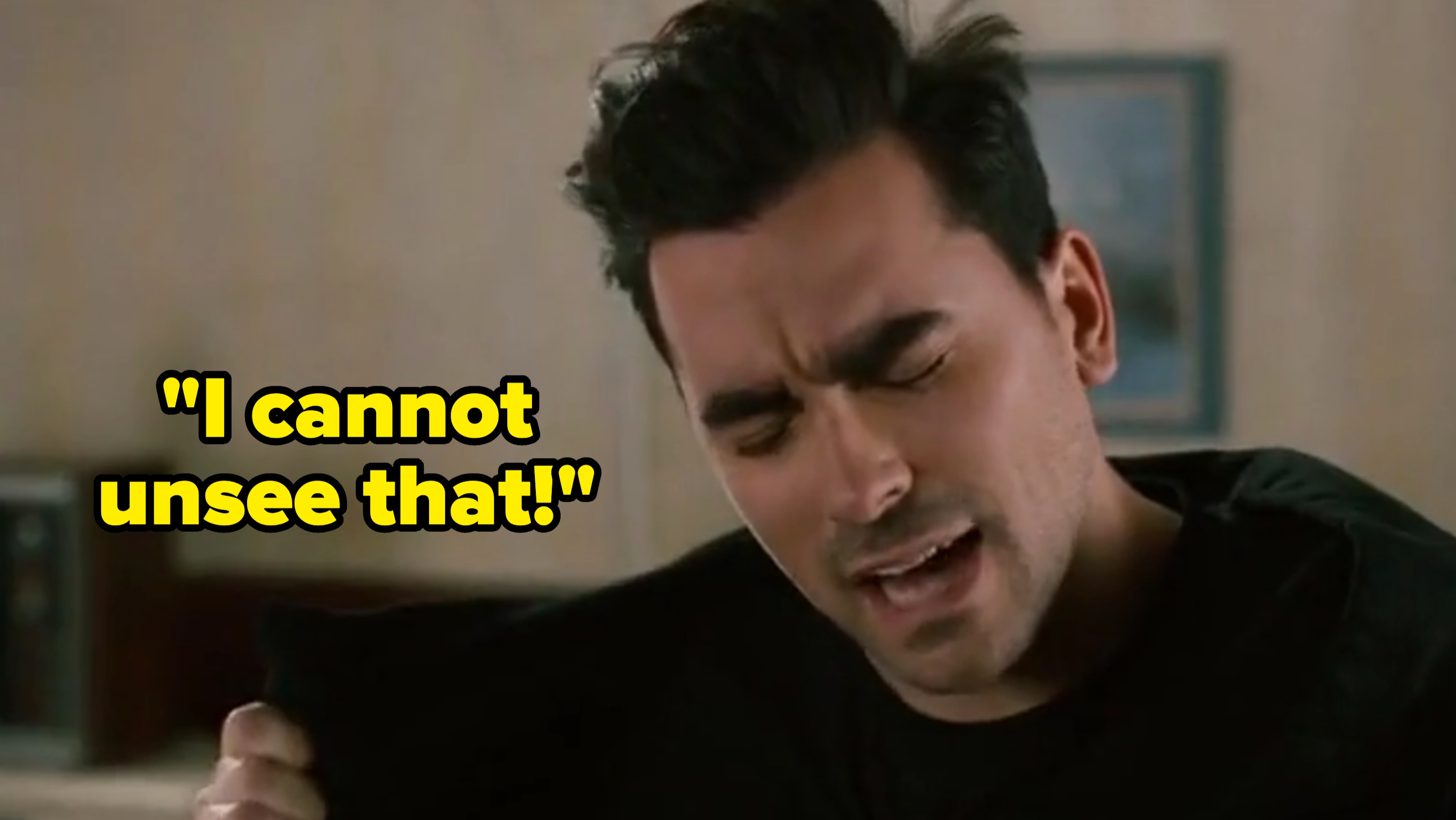 Person with closed eyes and expressive face, pulling at a shirt. Indoor setting with blurred background