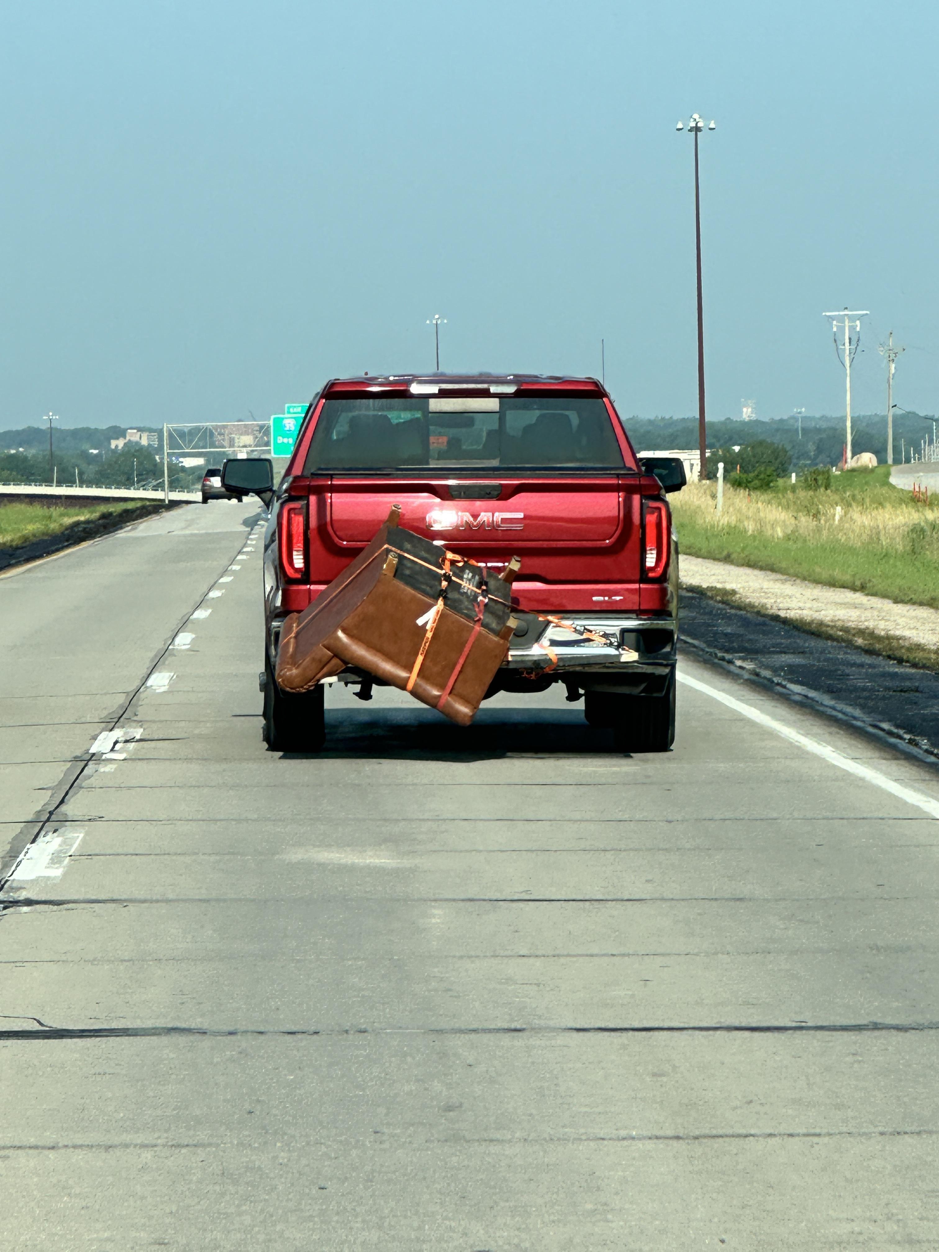 Pickup truck on a highway with a large armchair precariously attached to its open tailgate