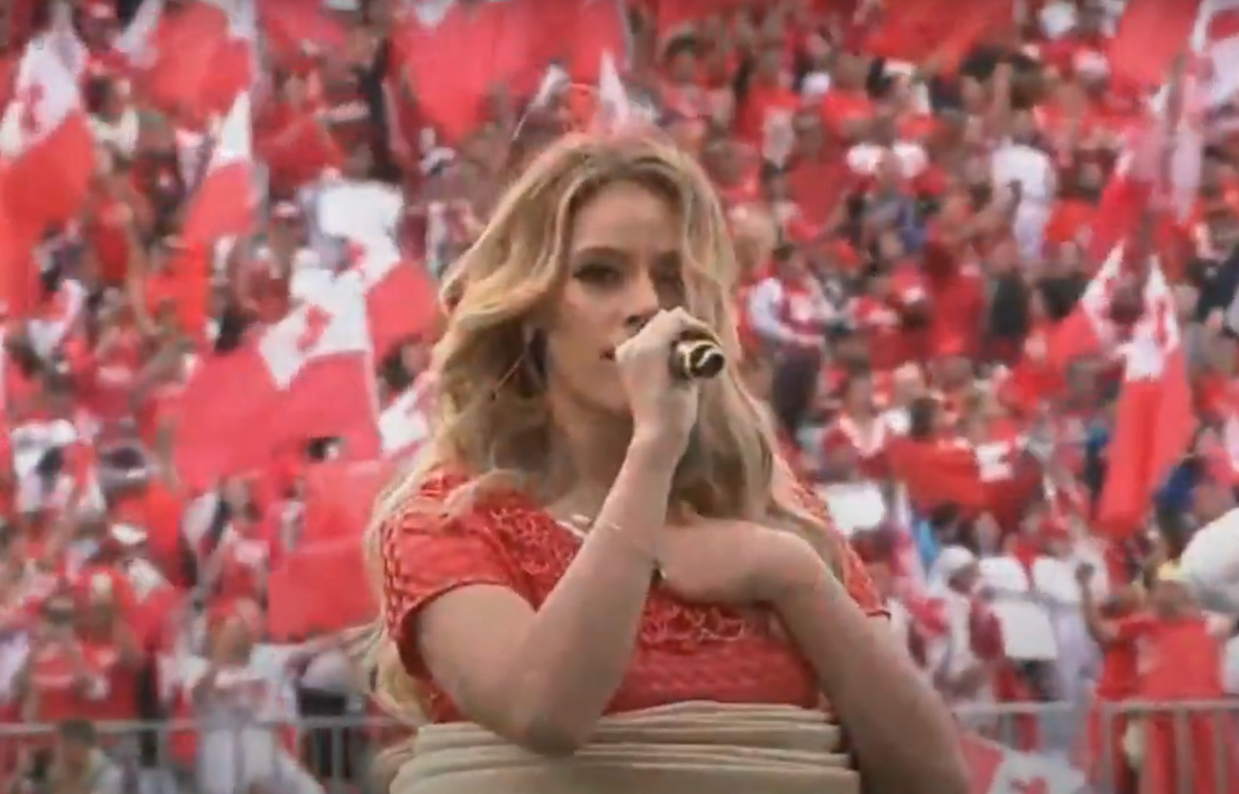 Person singing into a microphone at a large event, surrounded by a cheering crowd