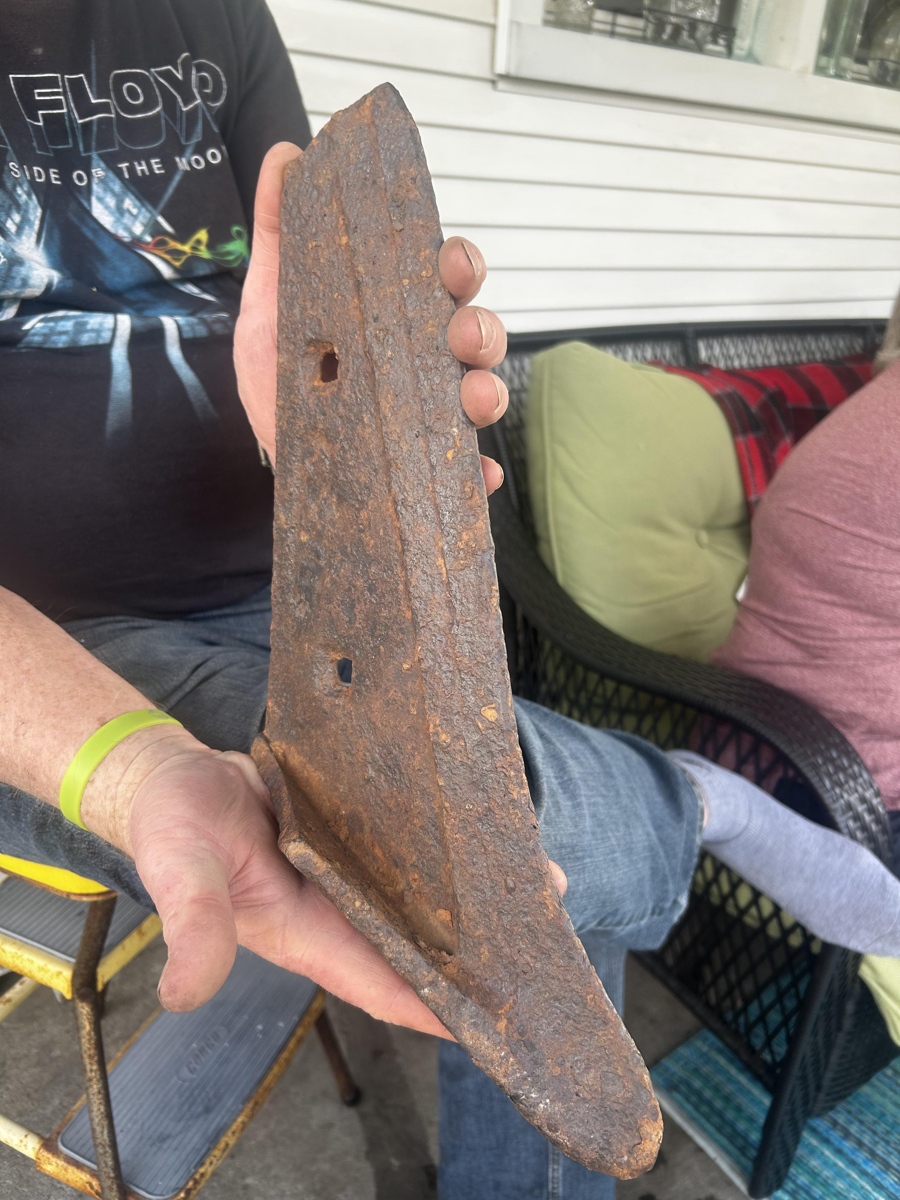 Person holding a large, rusted metal piece shaped like a wedge, sitting on a porch