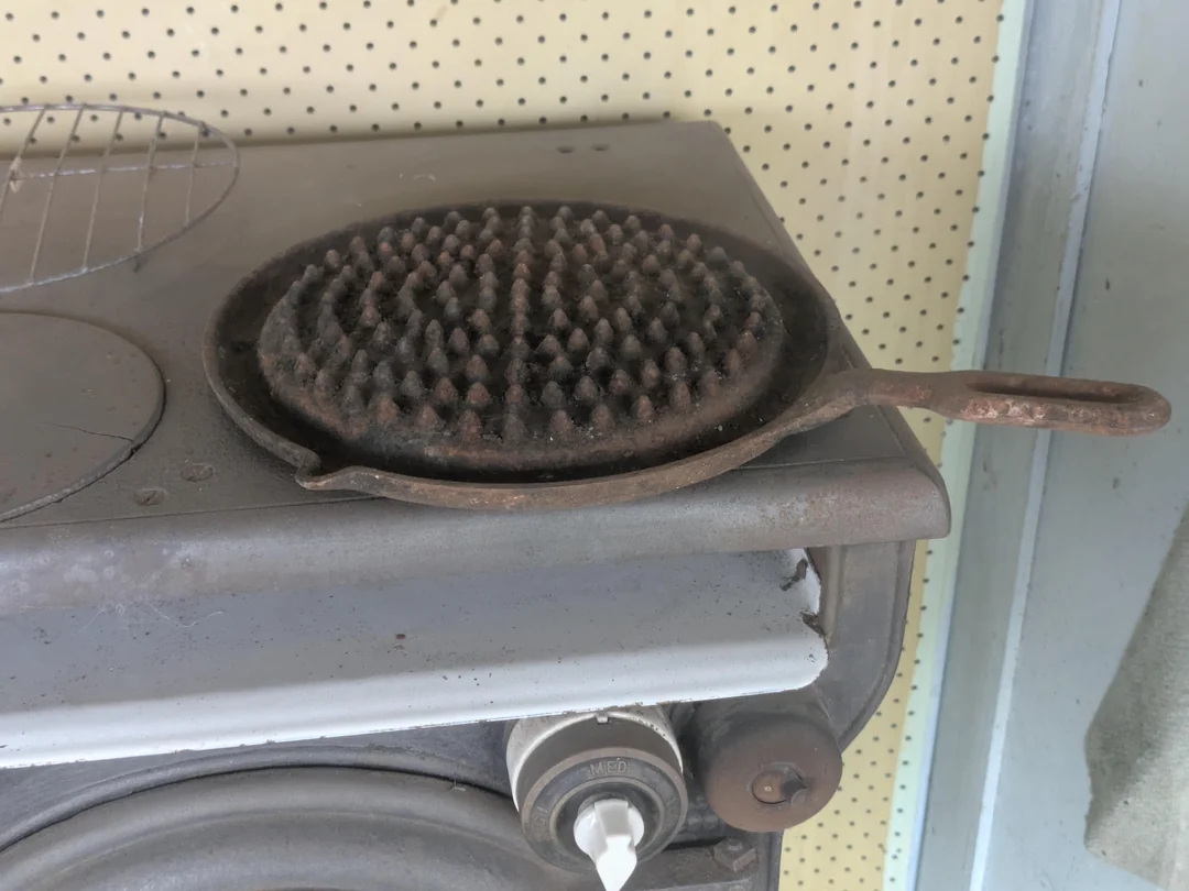 A round, spiked cast iron trivet sits on an old stove, used for supporting hot pots or pans