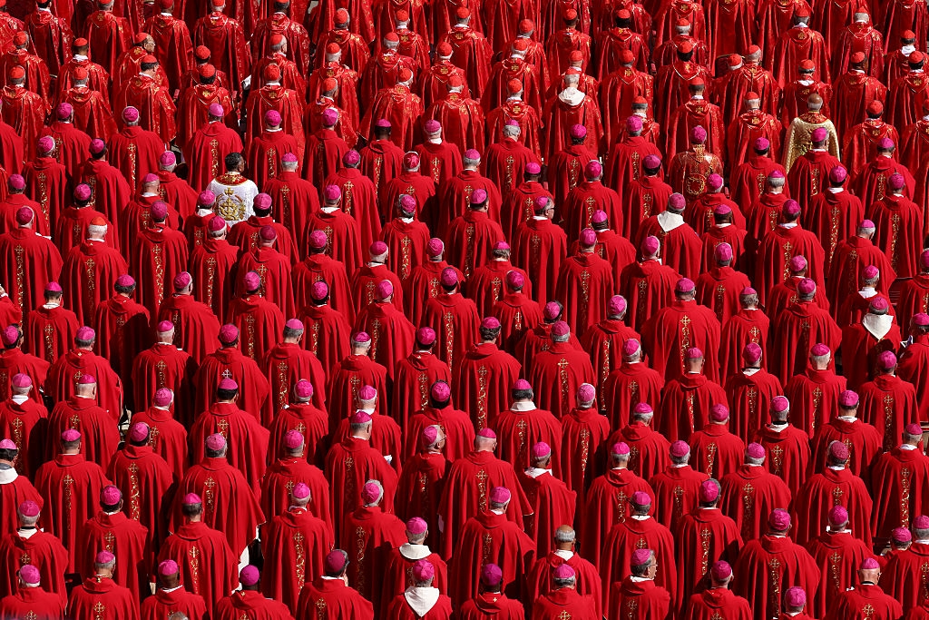 Many clergy wearing identical robes and hats stand together, seen from above during a formal gathering