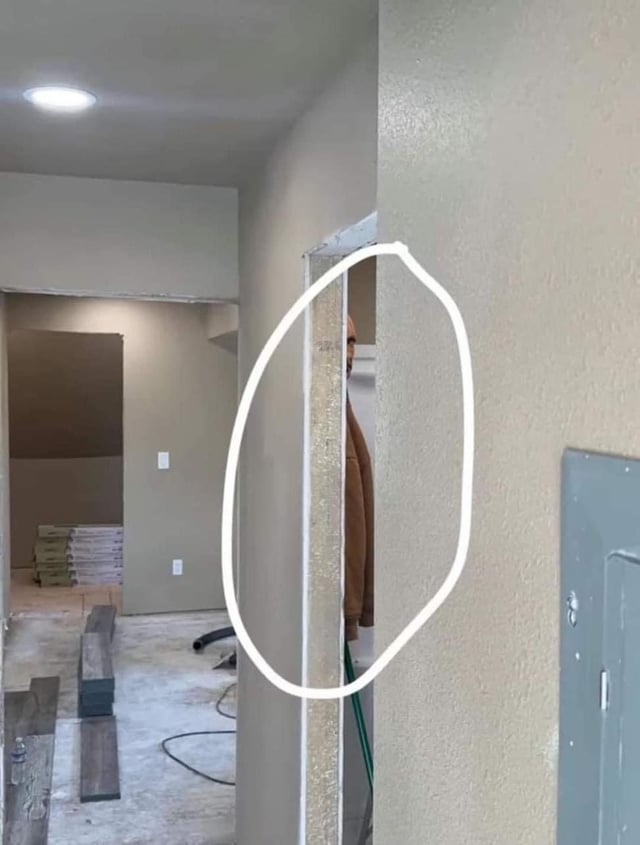 A person is partially hidden behind a wall in an under-construction room, with construction materials and tools in the background